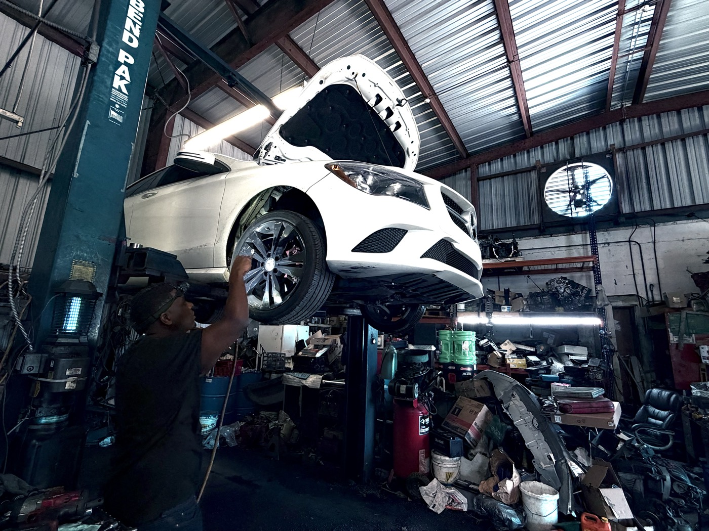 Technician working near the wheel area of a raised Mercedes-Benz at Front Line Auto